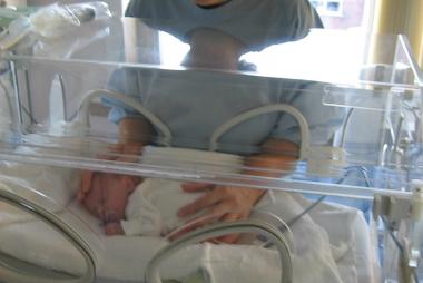 Mama in hospital smock places hands on baby in incubator