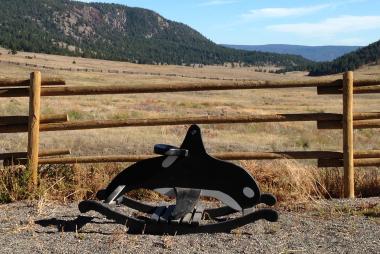 Wooden rocking orca toy against a backdrop of fence, field and mountain