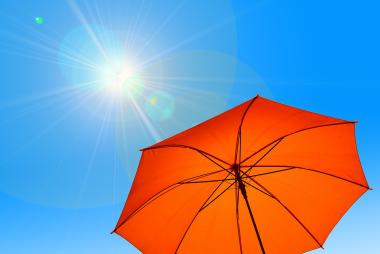Orange umbrella against brilliant blue sky with sun