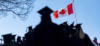 Graduates in cap and gown silhouetted against blue sky with Canadian flag