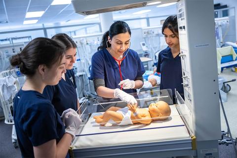 Certified Sim Nurse Educator instructs three students over a baby sim