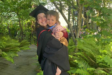 Roberta Watts in graduation regalia holds one of her children