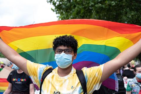 Young person holding rainbow flag, arms raised.