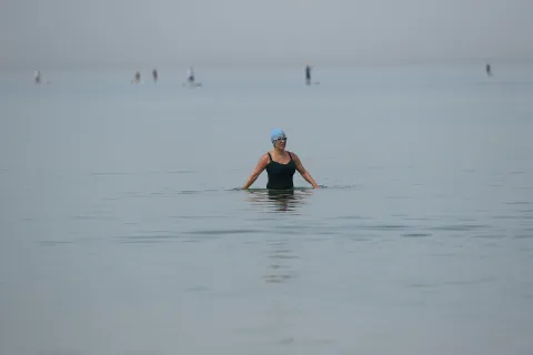 Woman with swim cap and goggles up to waist in water